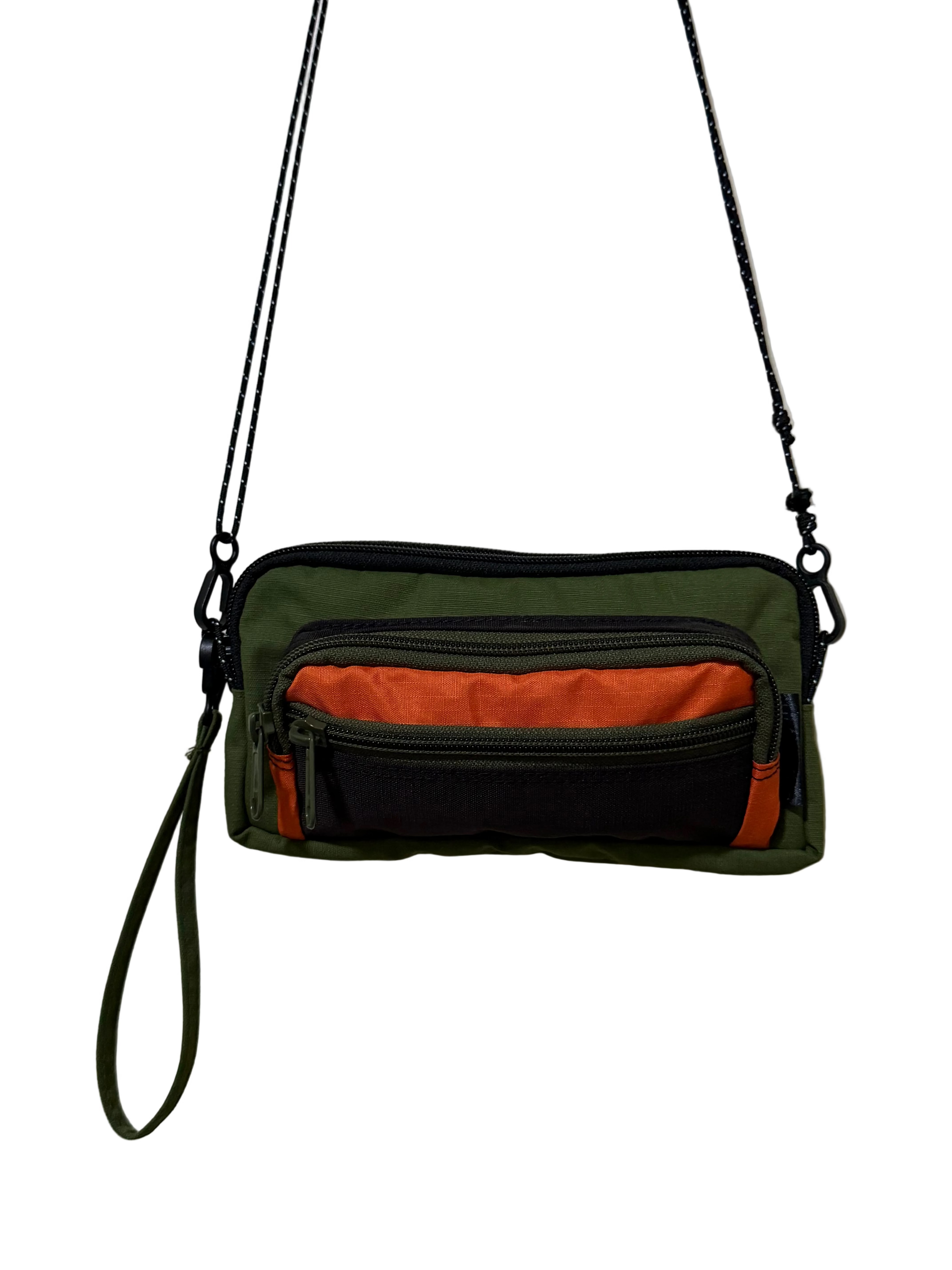 Green and black crossbody bag with orange interior on a white background